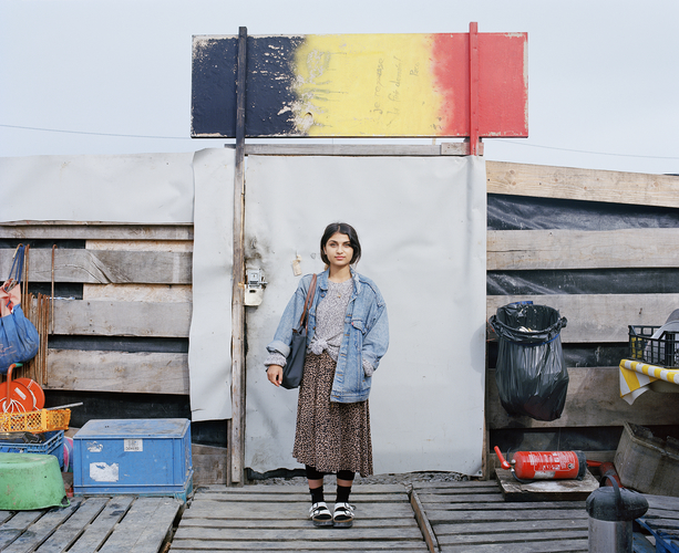 Elisa Larvego, Zara devant la porte de la Belgium kitchen, zone nord de la jungle de Calais, 2016, FNAC 2017-0053 (8), réalisée dans le cadre d’une commande publique photographique du Centre national des arts plastiques (Cnap) et du Pôle d’Exploration des Ressources Urbaines (PEROU) intitulée « Réinventer Calais » en 2016, Cnap © Elisa Lavergo / Cnap Elisa Larvego, Zara devant la porte de la Belgium kitchen, zone nord de la jungle de Calais, 2016, FNAC 2017-0053 (8), réalisée dans le cadre d’une commande publique photographique du Centre national des arts plastiques (Cnap) et du Pôle d’Exploration des Ressources Urbaines (PEROU) intitulée « Réinventer Calais » en 2016, Cnap © Elisa Lavergo / Cnap